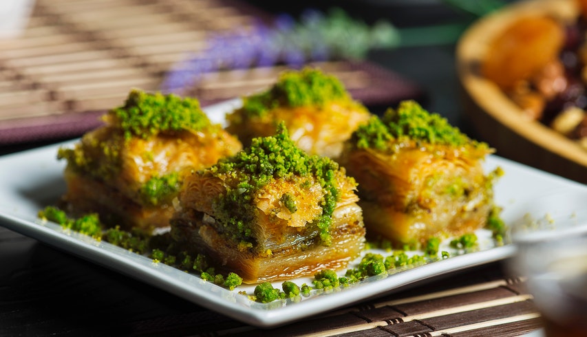 Four Baklava on a white plate topped with green pistachio nuts