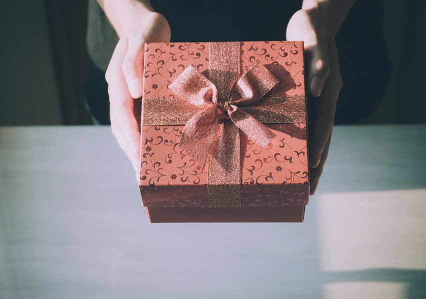 A picture showing the hands of someone passing a gift box